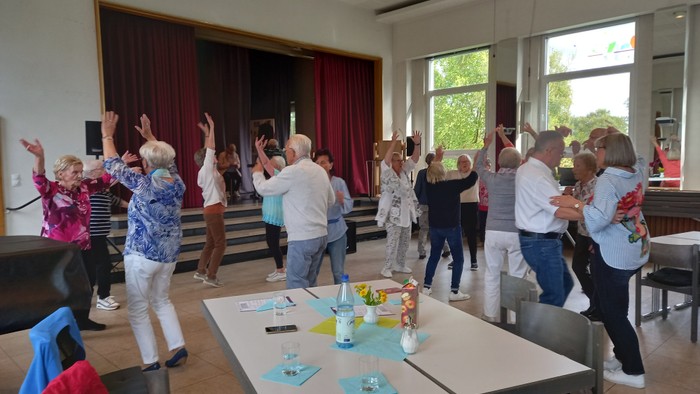 Gruppe von Menschen, die fröhlich an einer energiegeladenen Indoor-Sport- oder Tanzstunde teilnehmen.