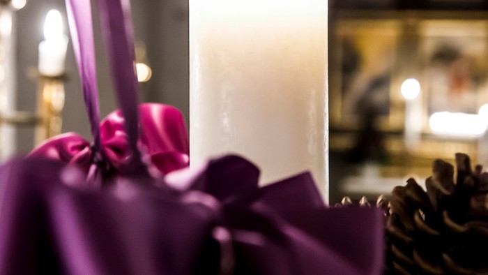 Elegant lilla blomster indrammer et tændt hvidt lys omgivet af festlige fyrredekorationer i en hyggelig stemning.