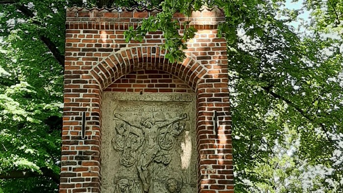 Ansicht einer Station des Lübecker Kreuzweges. In ummauerten Backsteinen wird auf einer Steinplatte die Kreuzigung Jesu dargestellt.