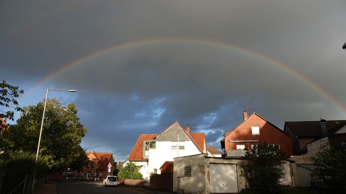 Ein Regenbogen spannt sich über ein Wohngebiet mit Häusern und Bäumen.