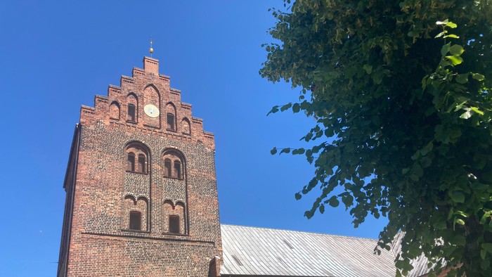 Røde murstenskirke med tårn og spids tak.
