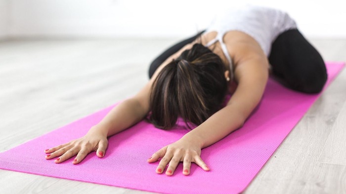 Ein Kind liegt auf einem pinken Yogateppich und ruht den Kopf auf den Armen.