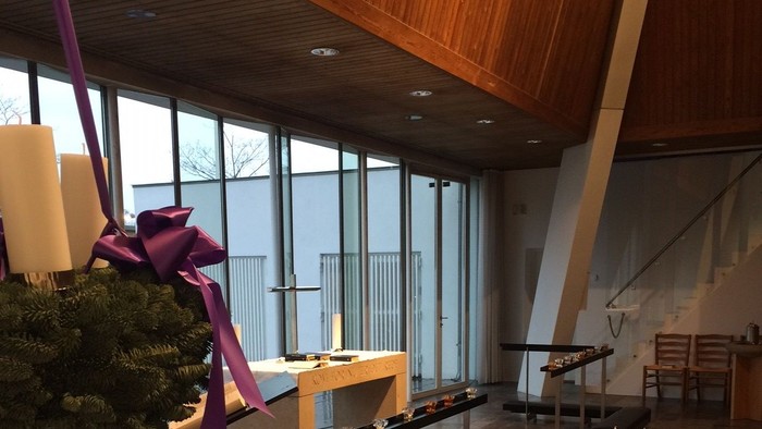 Indenrigspart af moderne kirke med adventskranse og lys.