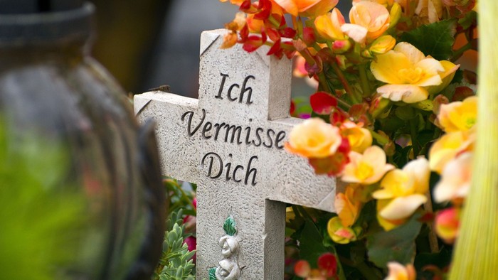 Ein herzliches Kreuz mit der Inschrift *„Ich vermisse dich“*, umgeben von lebendigen Blumen.