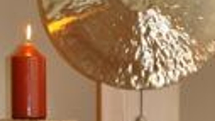 Eine brennende Kerze steht neben einem dekorativen Metallgegenstand und einer weißen Vase.