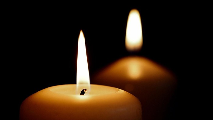 Zwei brennende Kerzen mit hellen Flammen vor dunklem Hintergrund.