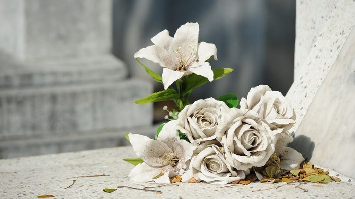 Elegante weiße Rosen und Blüten liegen verstreut nahe einem Grabstein auf einem Marmorboden.