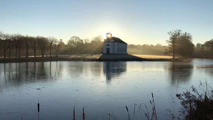 En lille kirke på en liten ø i en sø med solopgang i baggrunden