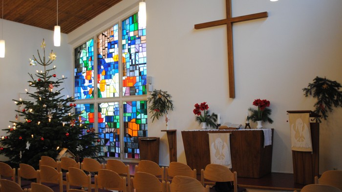In der Kirche stehen Weihnachtsbaum, Kreuz und bunte Fenster.