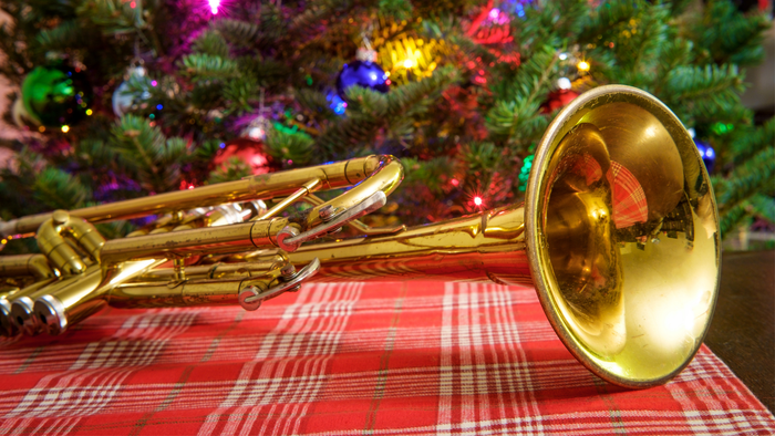 Ein goldenes Blechblasinstrument liegt vor einem Weihnachtsbaum.