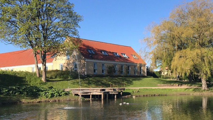 En rolig sø med et rødt taget hus og træer ved siden af