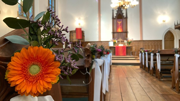 Blumenarrangement in Kirchenbank, Altar im Hintergrund