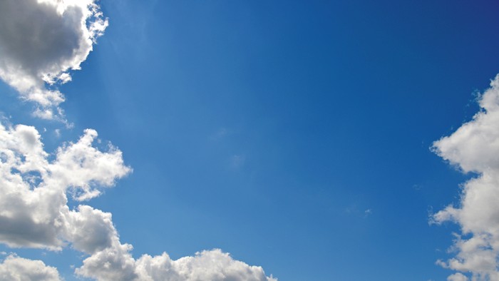 Heller blauer Himmel mit vereinzelten, flauschigen weißen Wolken unter klarem Sonnenlicht.