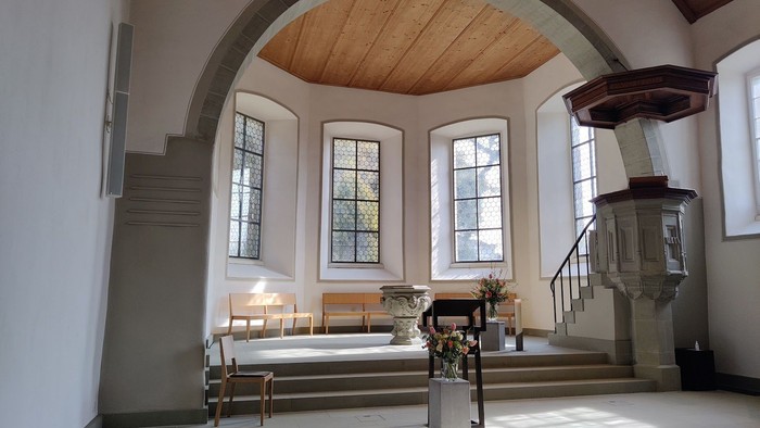 Hyggelig kirkeindretning med træbænke, farvede glasvinduer og en prædikestol under et hvælvet loft.