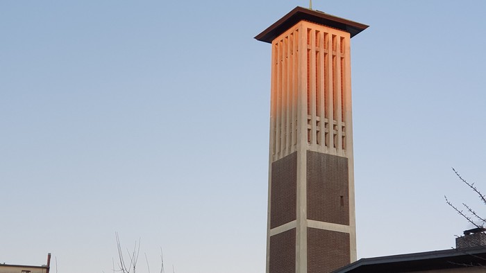 Der Kirchturm der Paul-Gerhardt-Kirche Altona wird im oberen Teil von der Abendsonne rötlich angestrahlt. Auf der Turmspitze ist der Wetterhahn zu sehen. Im unteren Teil sind Fenster des Anbaus zu sehen.