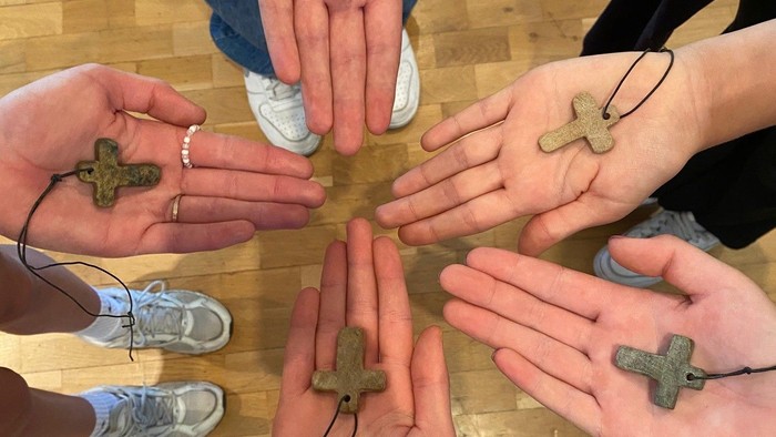 Eine Gruppe von Händen, die kleine Steinkreuze halten, die durch Schnüre in einer Kreisformation verbunden sind.