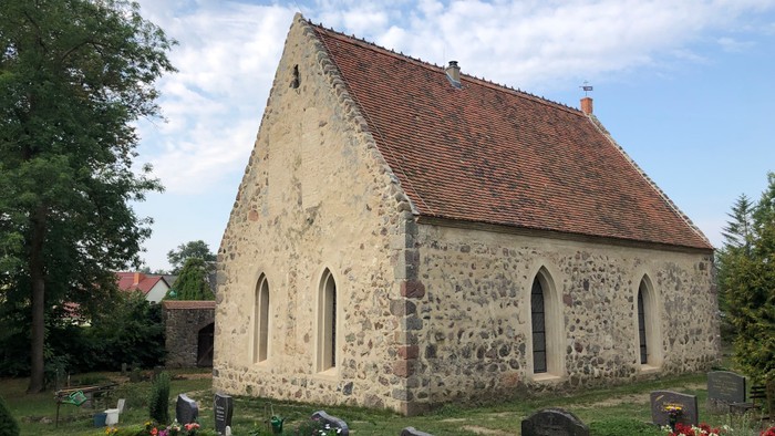 Historische Steinkapelle, umgeben von einem ruhigen, gepflegten Friedhof mit Gräbern und Blumen.