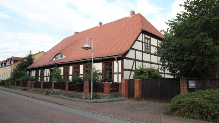 Traditionelles Fachwerkhaus mit rotem Ziegeldach in einer ruhigen, gepflasterten Straße.