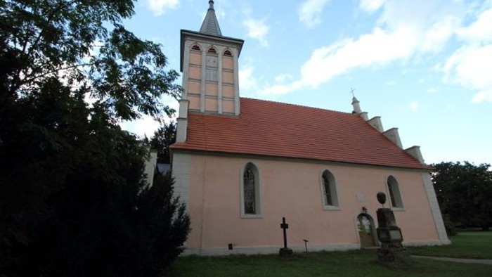 Idyllische Kirche mit rotem Dach und Glockenturm in einer ruhigen, grünen Landschaft.