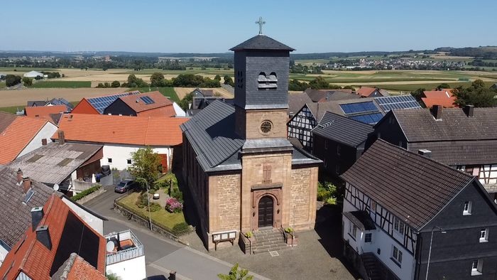 Kirchturm mit Uhr und Kreuz, umgeben von Häusern und Feldern