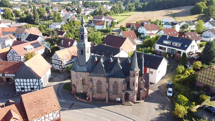 Das Bild zeigt eine historische Kirche in einem kleinen Dorf mit umliegenden Häusern.