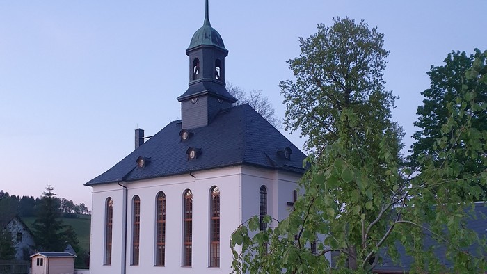 Kirche mit Friedhof und Bäumen im Hintergrund