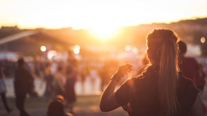 Eine Frau mit langen Haaren tanzt bei einem Festival bei Sonnenuntergang.