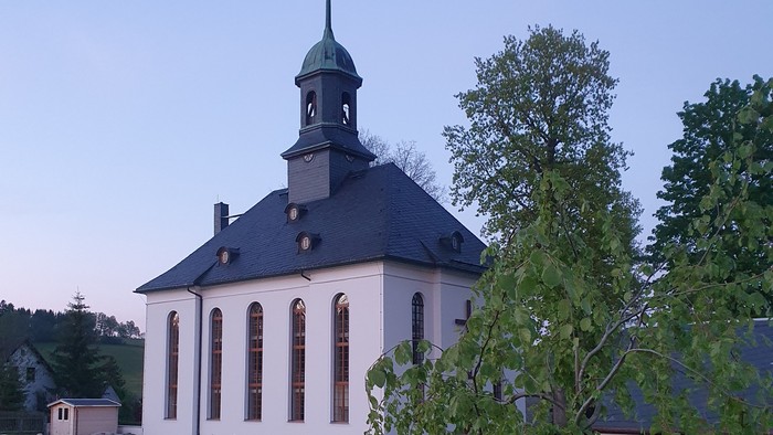 Kirche mit Friedhof und Bäumen im Hintergrund