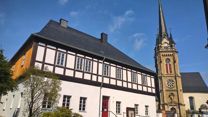 Traditionelles Fachwerkgebäude neben einer historischen Kirche mit einem hohen, verzierten Turm.