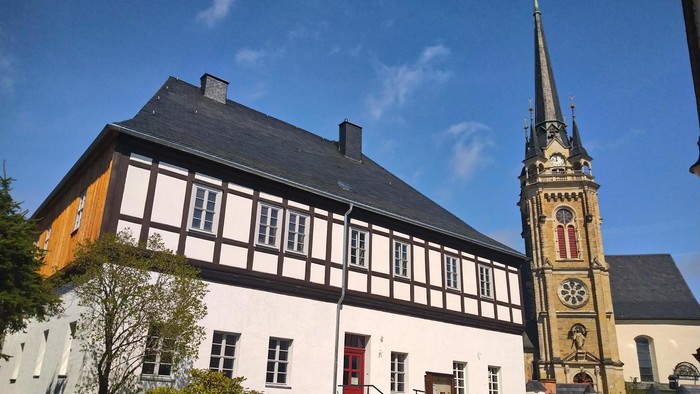 Traditionelles Fachwerkgebäude neben einer historischen Kirche mit einem hohen, verzierten Turm.