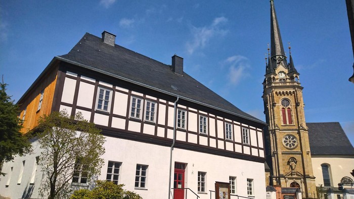 Traditionelles Fachwerkgebäude neben einer historischen Kirche mit einem hohen, verzierten Turm.