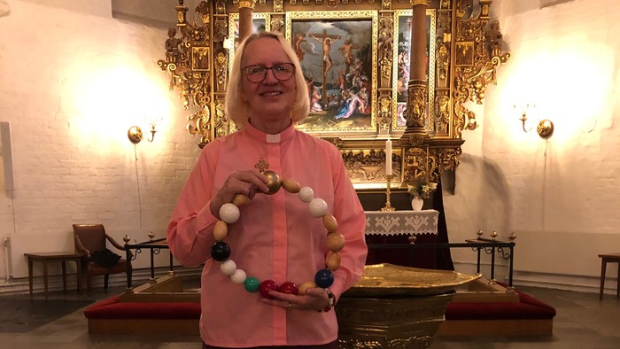 Kvinde i rosa bluse holder en kæde af kugler i kirke.