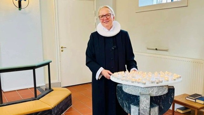 En person i religiøst tøj tænder lys ved et lysestage i en rolig kapelsal.