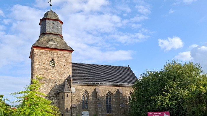Historische Steinkirche mit hohem Glockenturm in einer üppigen, grünen Landschaft.