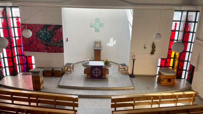 Moderner Kapelleninnenraum mit hölzernen Kirchenbänken, zentralem Altar, Buntglasfenstern und minimalistischem Dekor.
