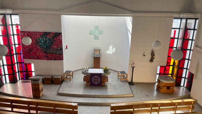 Moderner Kapelleninnenraum mit hölzernen Kirchenbänken, zentralem Altar, Buntglasfenstern und minimalistischem Dekor.