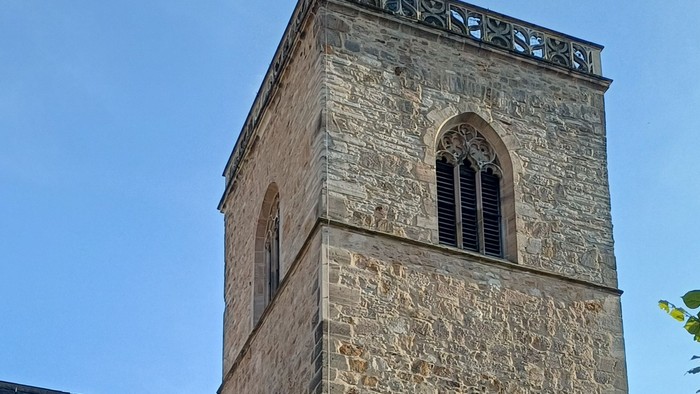Historische Steinkirche mit hohem Glockenturm und einem geparkten roten Auto davor.