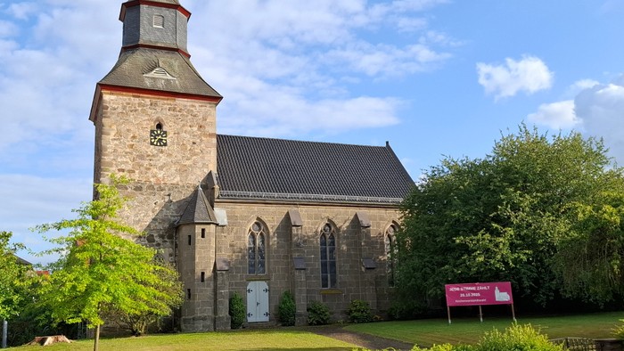 Historische Steinkirche mit hohem Glockenturm in einer üppigen, grünen Landschaft.
