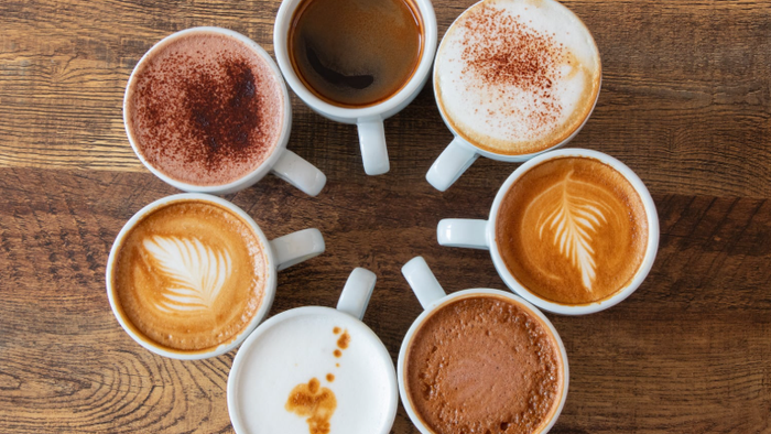 Syv forskellige kaffedrikke arrangeret kunstnerligt i et cirkulært mønster på en træoverflade.