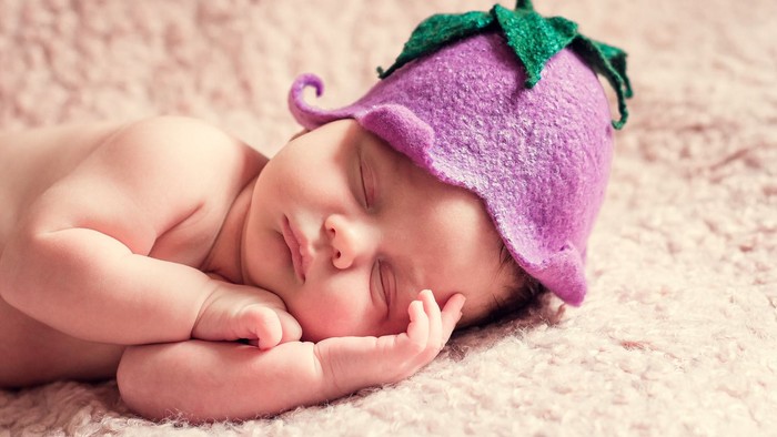 Ein schlafendes Baby mit einer lila Strumpfhut-Mütze mit grünen Blättern.