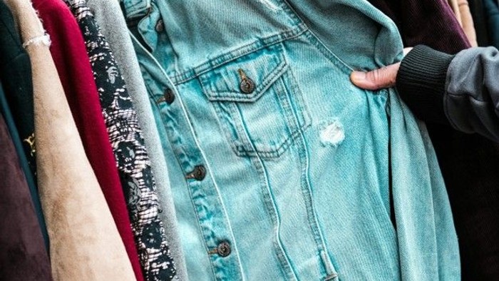 Lyseblå denimjakke med studsede manchetter og patches på en tøjstativ.