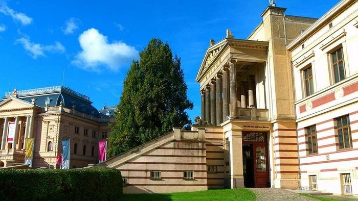 Eleganter neoklassizistischer Bau mit imposanten Säulen und Treppen, die an einem sonnigen Tag zu einem Eingang führen.