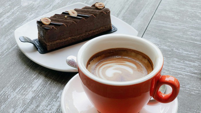 Lækkert chokoladedessertstykke serveret med en latte i en livlig rød kop på en underkop.
