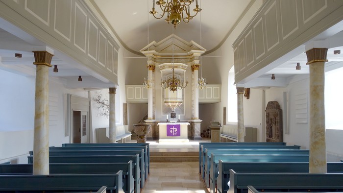 Die Kirche hat blaue Bänke und weiße Säulen.