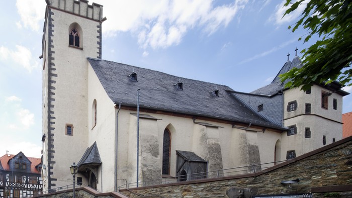Historische Kirche mit hohem Turm und angrenzender Steinfestung am Hang.