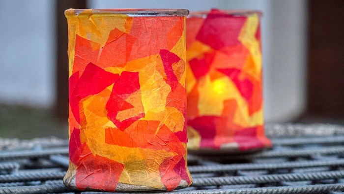 Zwei bunte, mit Seidenpapier bedeckte Kerzen auf einer Metalloberfläche.