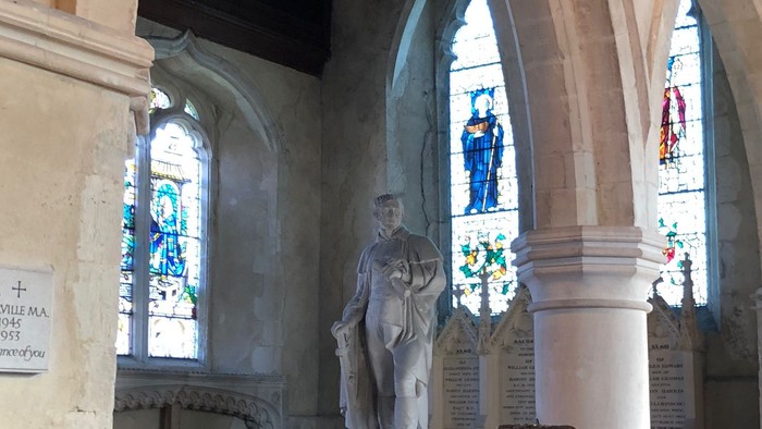 Gothic church interior featuring a statue, stained glass windows, and ornate pews.