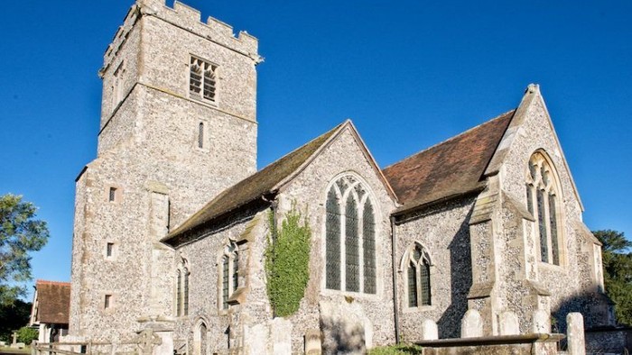 Stone church with tall tower and arched windows, surrounded by gravestones under a clear blue sky.