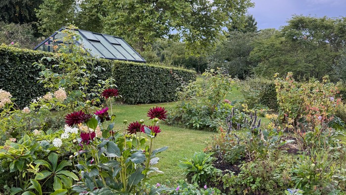 Frodig have fyldt med farverige blomster, grønt og et charmerende glashus i baggrunden.