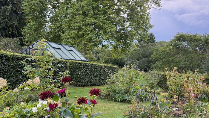 Frodig have fyldt med farverige blomster, grønt og et charmerende glashus i baggrunden.